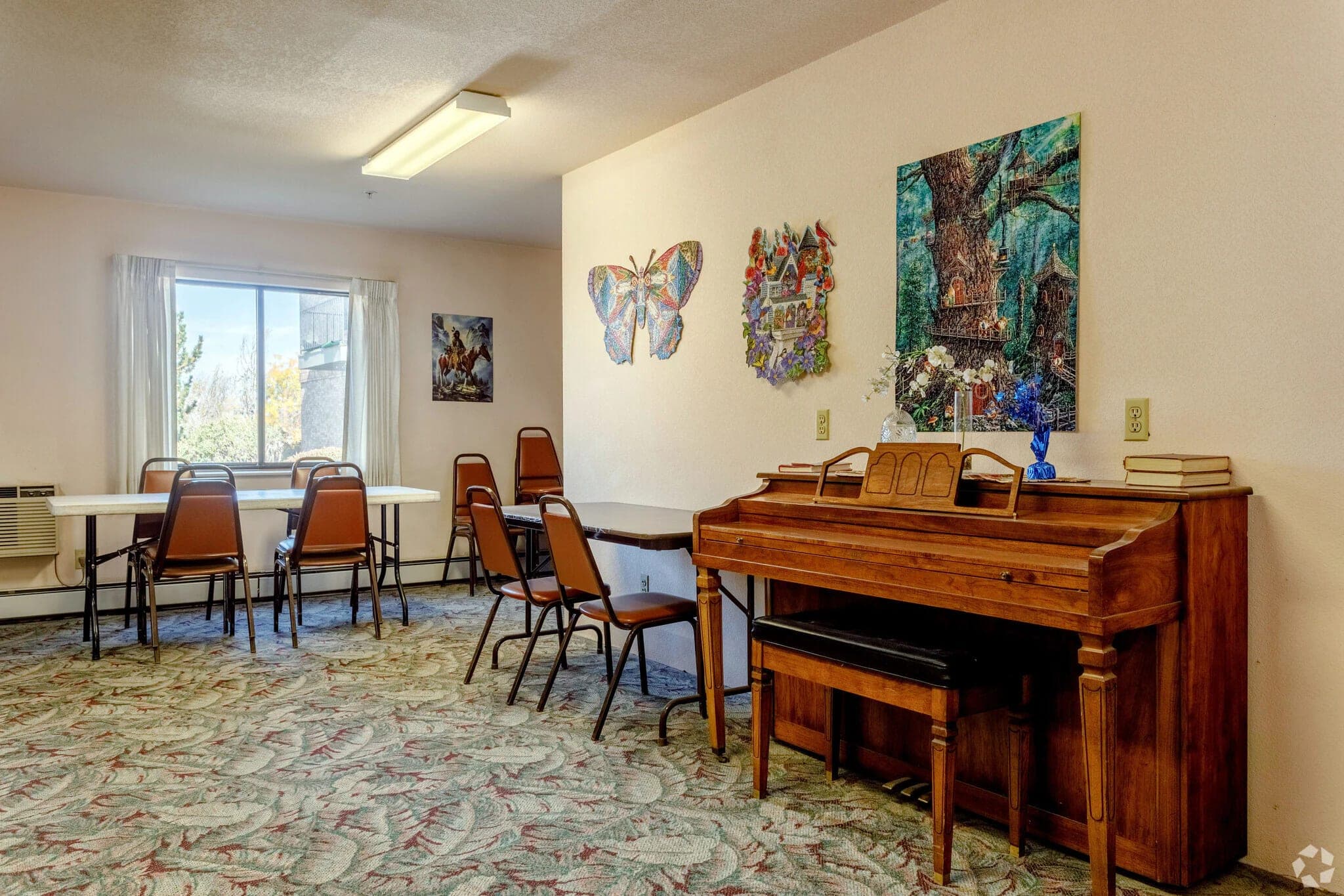 The activity room, with a piano against one wall, residents’ artwork hung above it, and tables set up by the window.