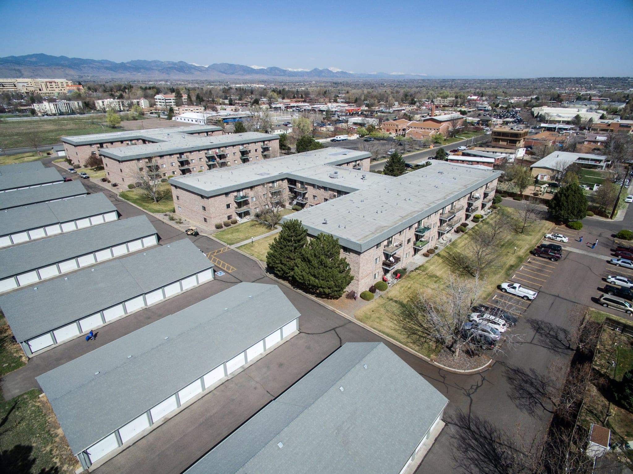 Morningside from the air: three long apartment buildings and two rows of private garages around their own parking, with Wheat Ridge spread out beyond and the Rocky Mountains along the horizon.