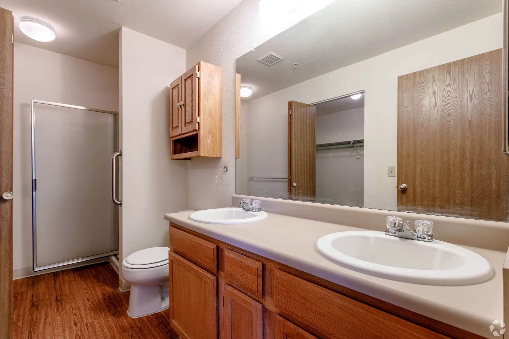 A second bathroom with a step-in shower stall with a grab bar, a double-sink vanity with oak cabinets, and a full-width mirror.