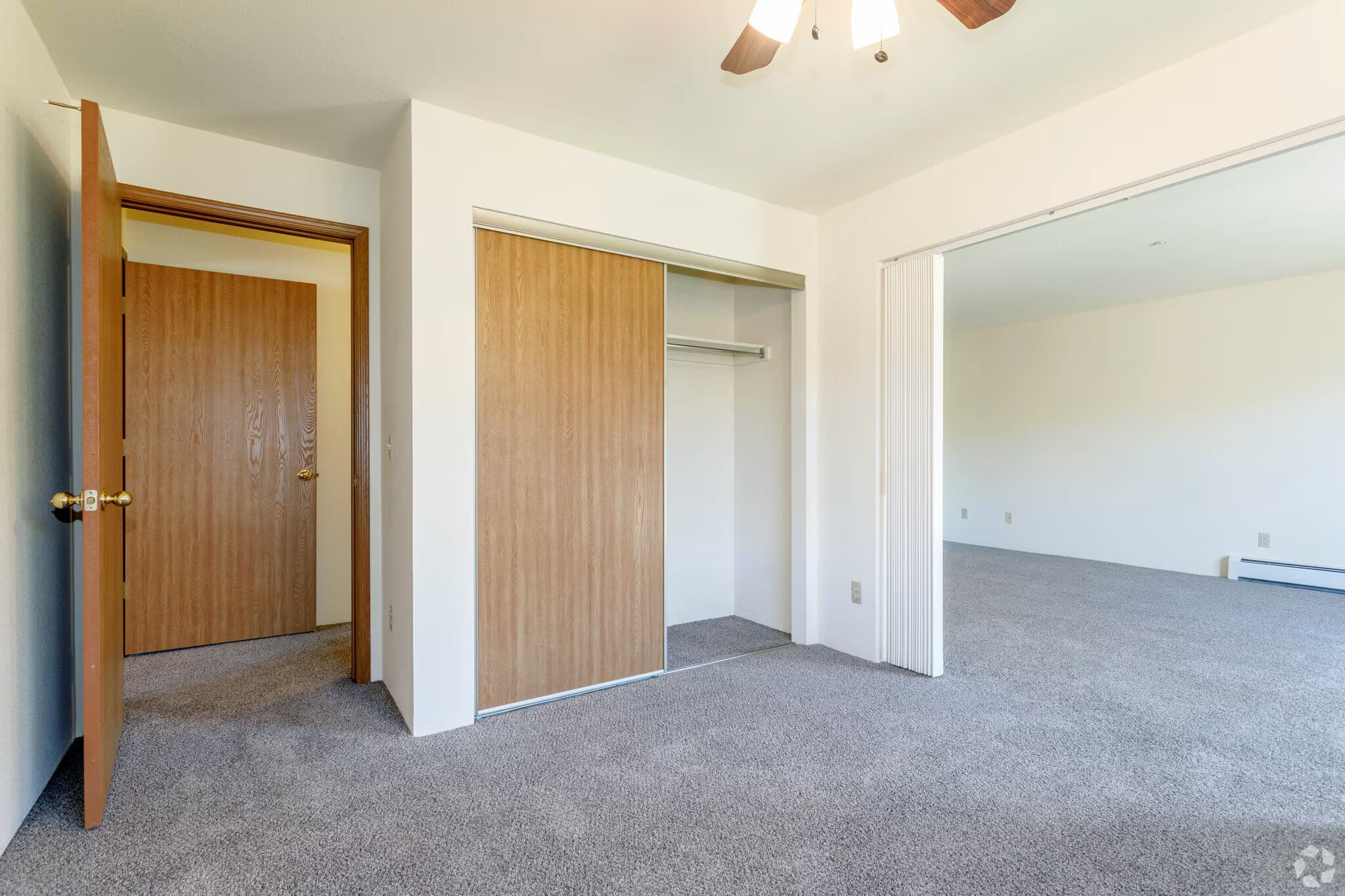 A carpeted bedroom with a wide sliding-door closet, a ceiling fan with a light, and a folding partition to the living room.