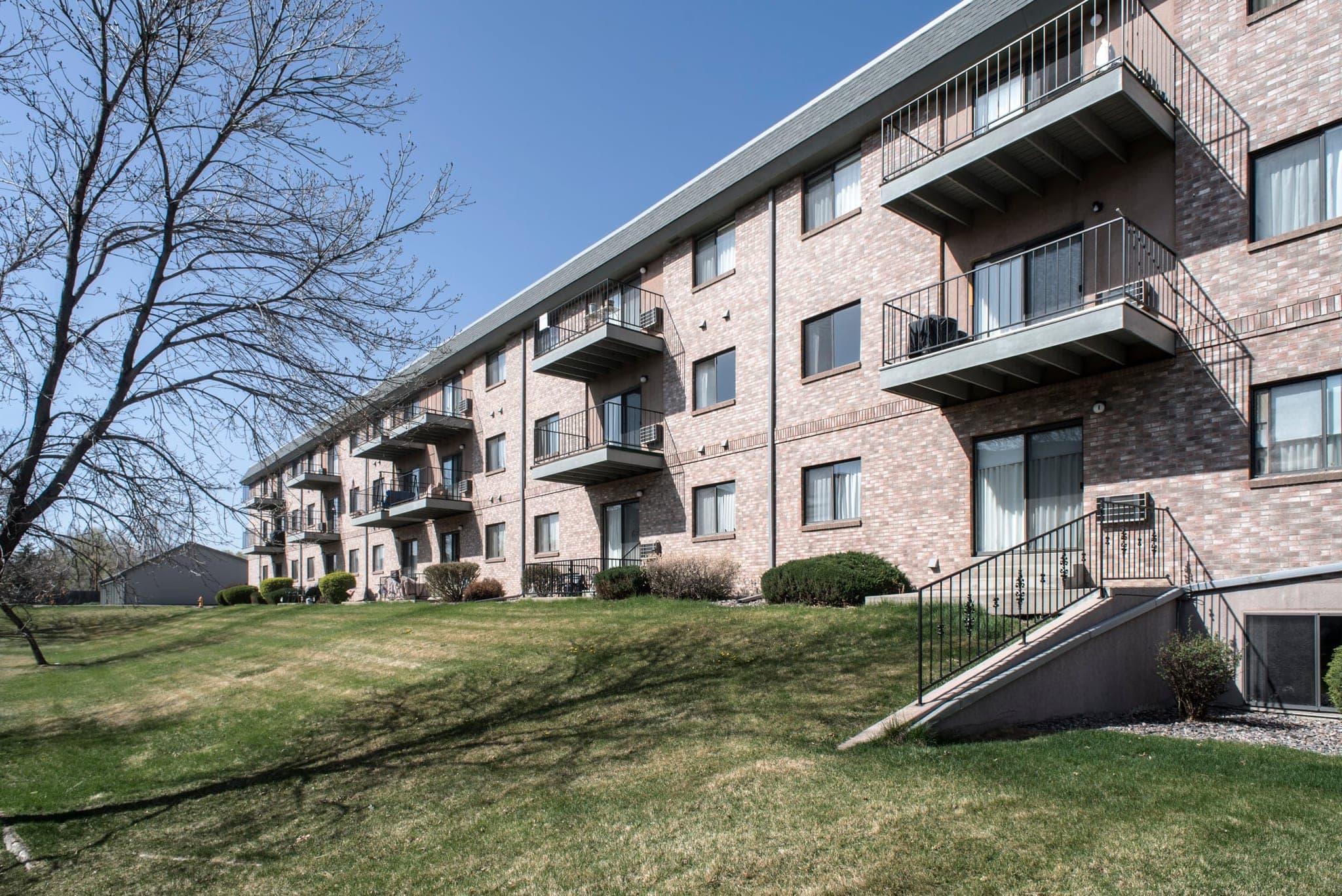 The end of one Morningside building under a clear blue sky, showing stacked private balconies, a railed stair down to the garden level, and lawn running up to the wall.