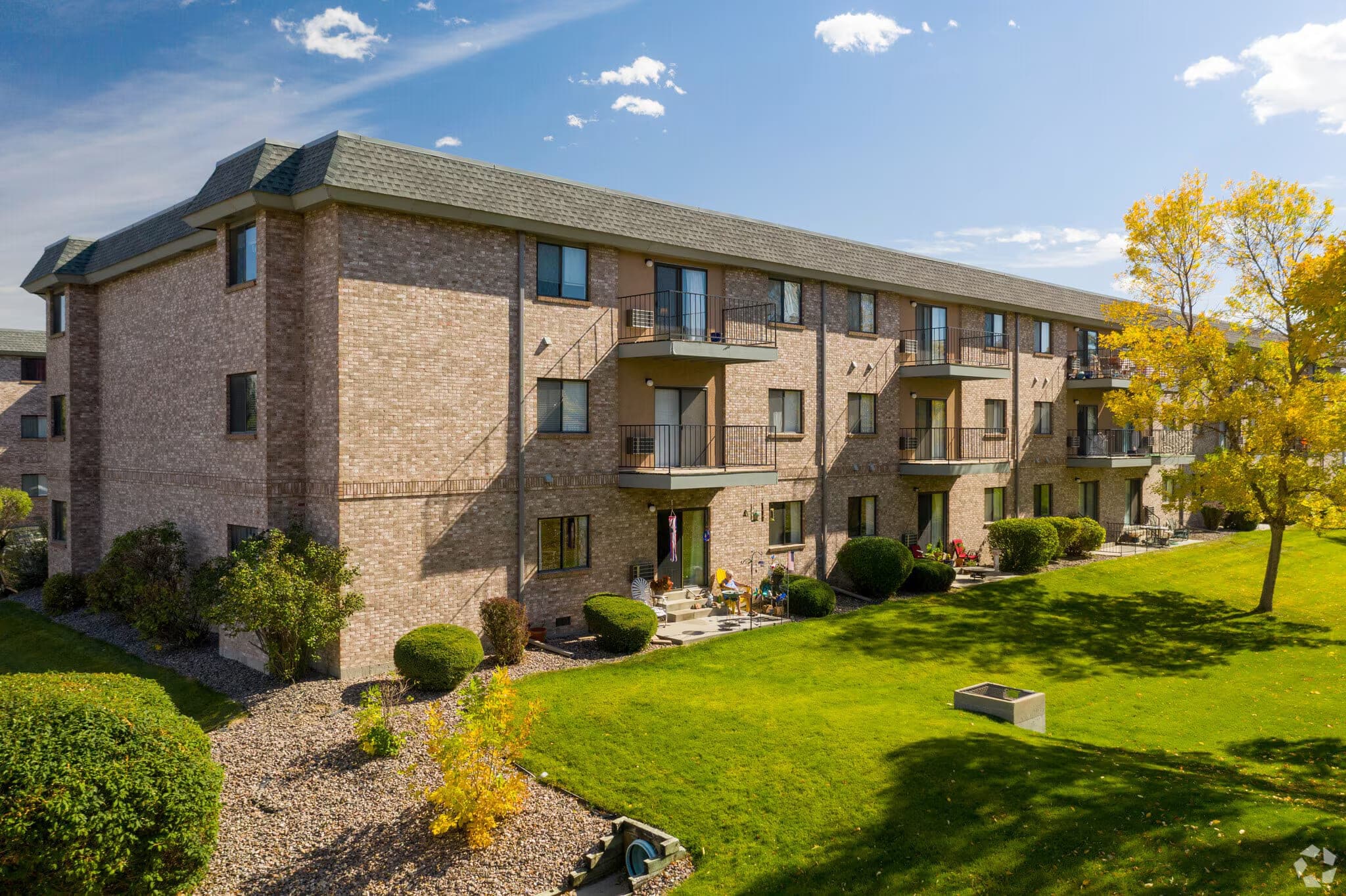 A three-storey brick apartment building at Morningside, with private balconies and patios overlooking a mown lawn and autumn trees.