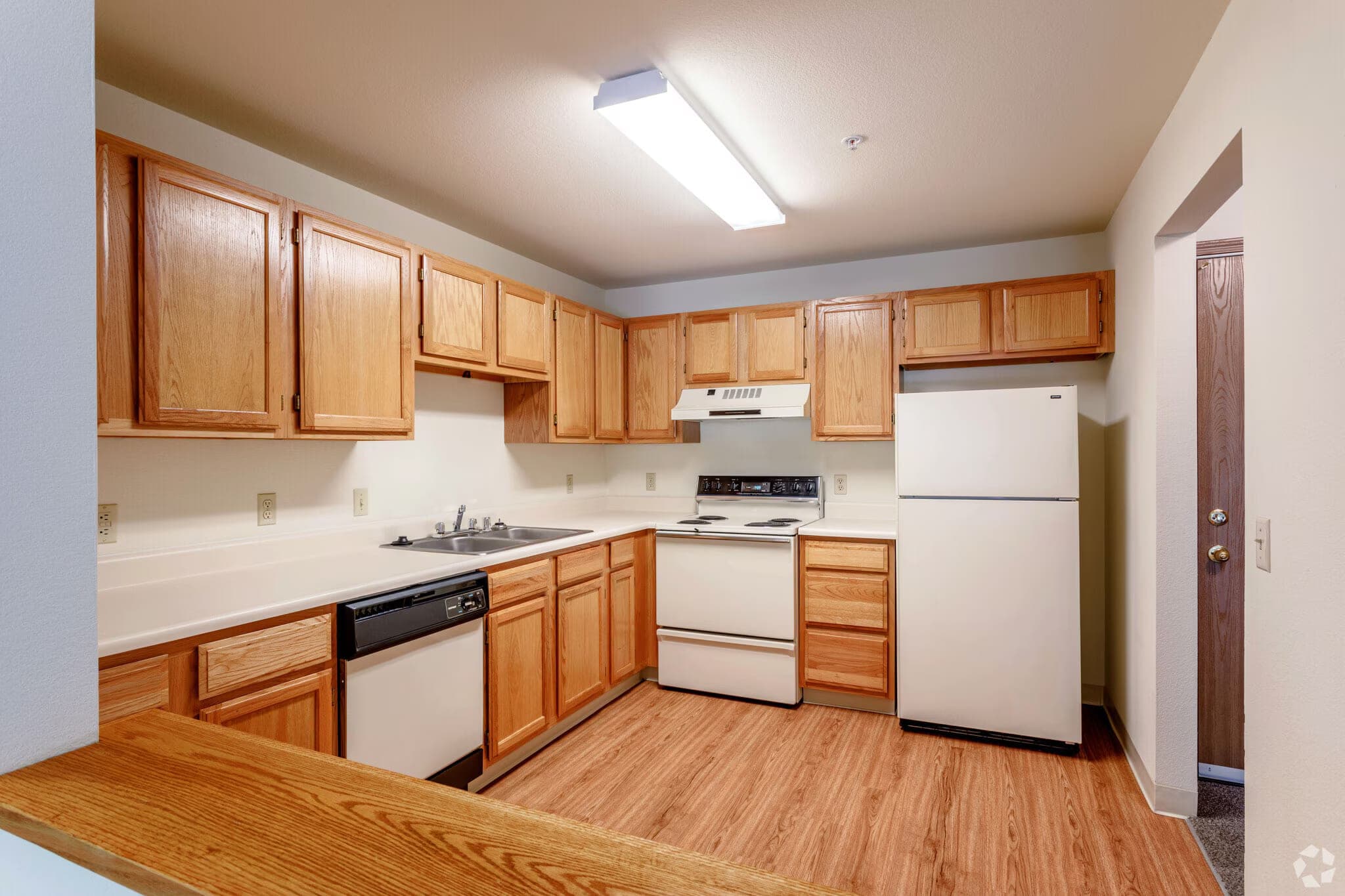 A kitchen with oak cabinets to the ceiling, an electric range, dishwasher, full-size refrigerator, double-basin sink and a breakfast bar.