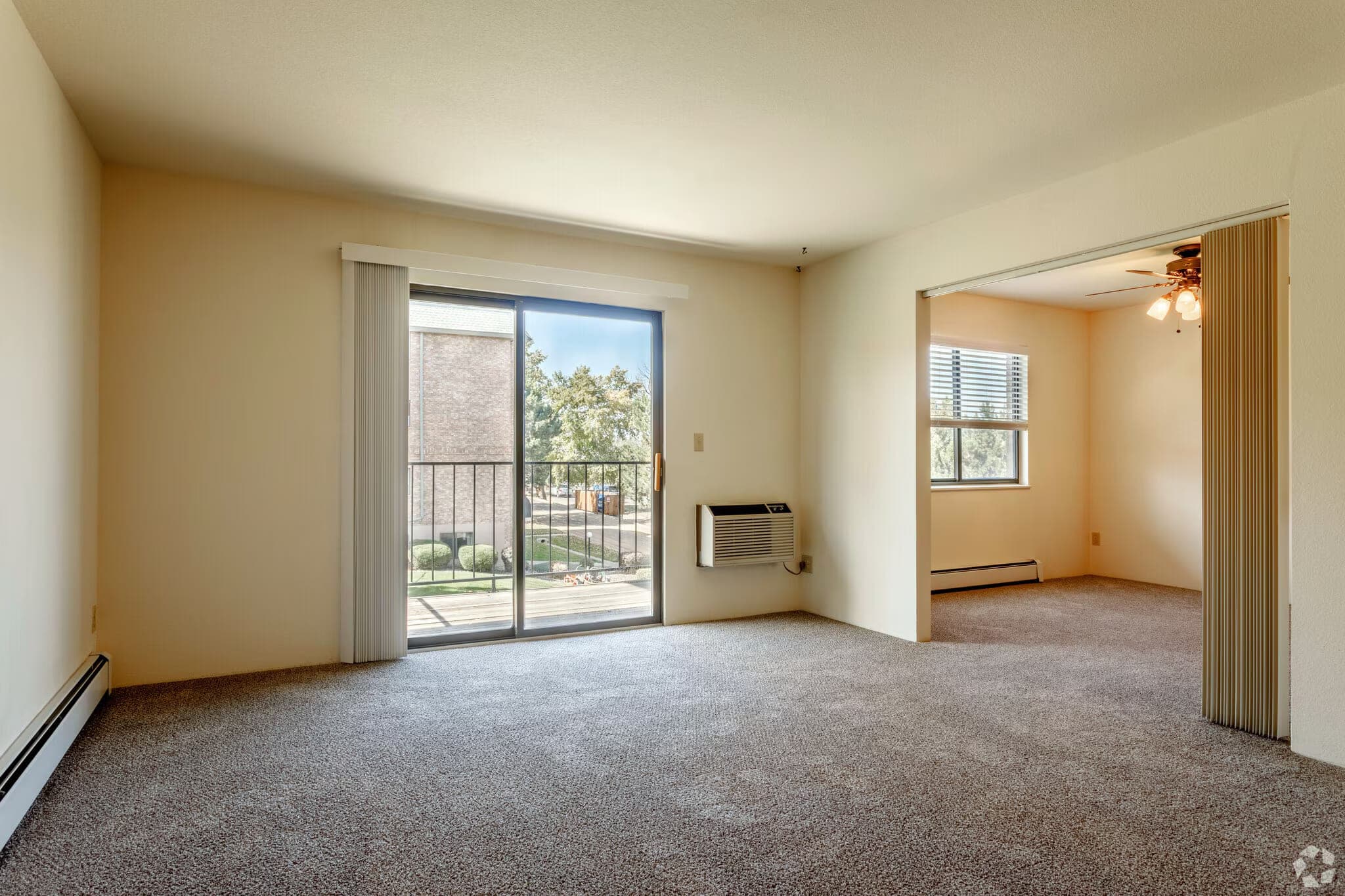 A living room with a sliding glass door onto the balcony, opening through to a second room with a ceiling fan.