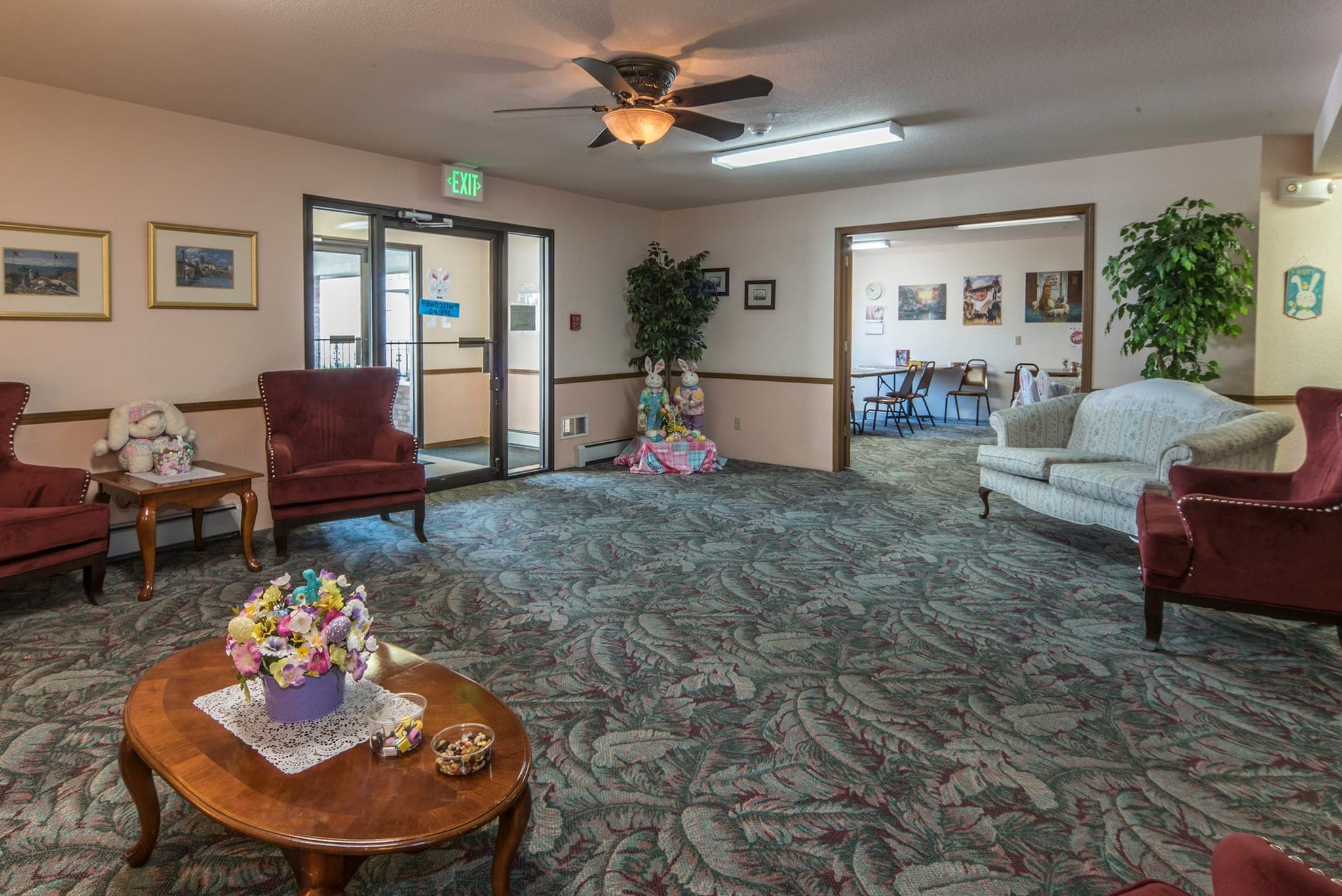 The lobby, with armchairs and a sofa arranged around a low round table of flowers, pot plants and framed pictures, and glass entrance doors letting in the light.